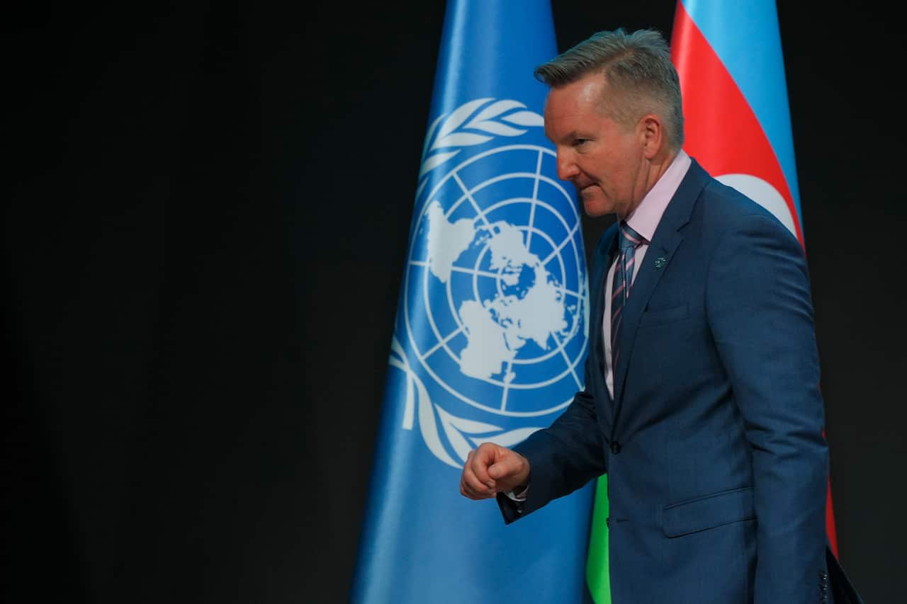 A man in a blue suit is walking in front of two flags.