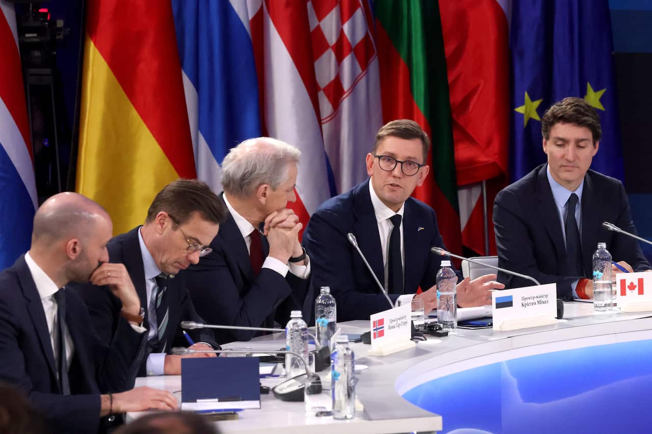 Five men in suits sitting at a curved table. There are different national flags behind them.