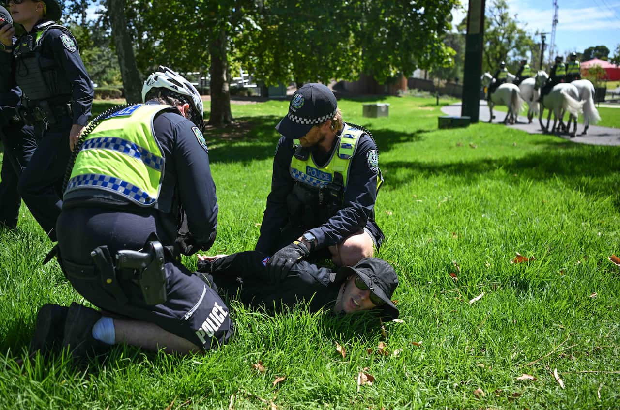 Two police officers in uniform restrain a person on the grass.