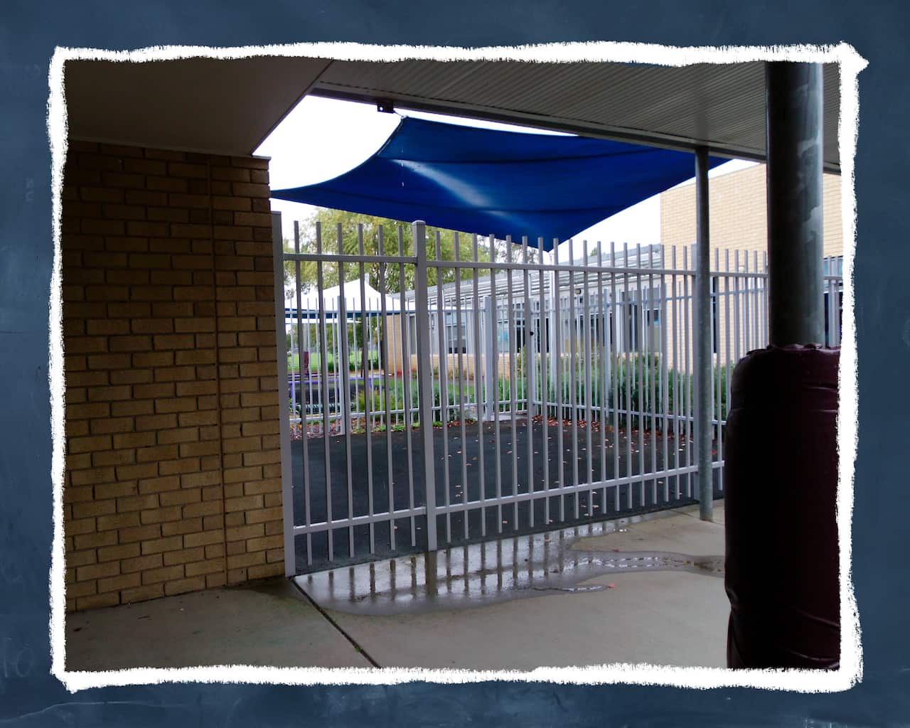 A small outdoor area at a school surrounded by a white fence and blue tarpaulin.