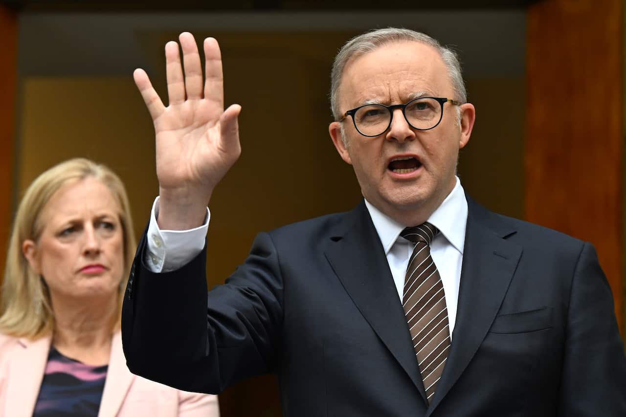 Anthony Albanese, wearing a suit and tie, holding his right hand up as he speaks.