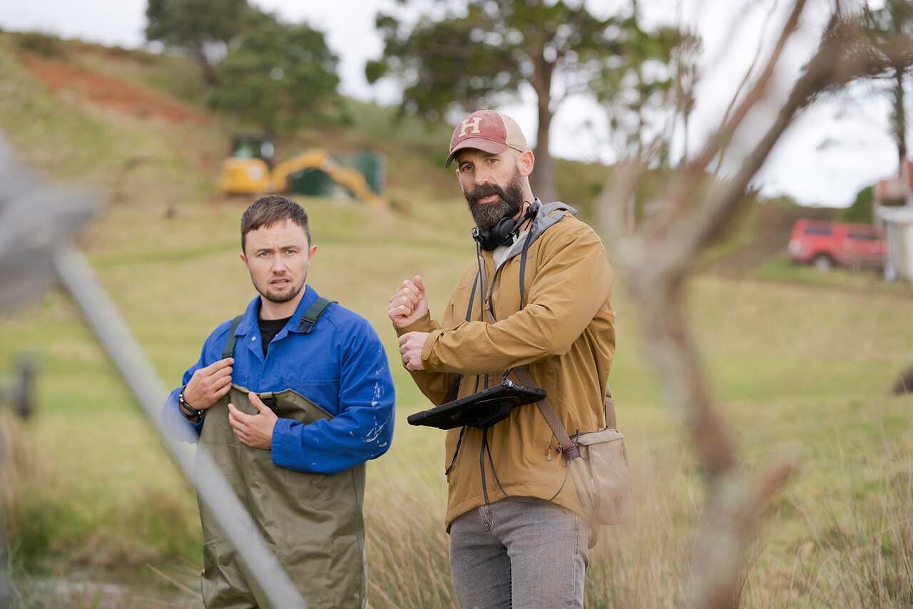Two men, actor Elz Carrad and showrunner Max Currie, stand in a field.  