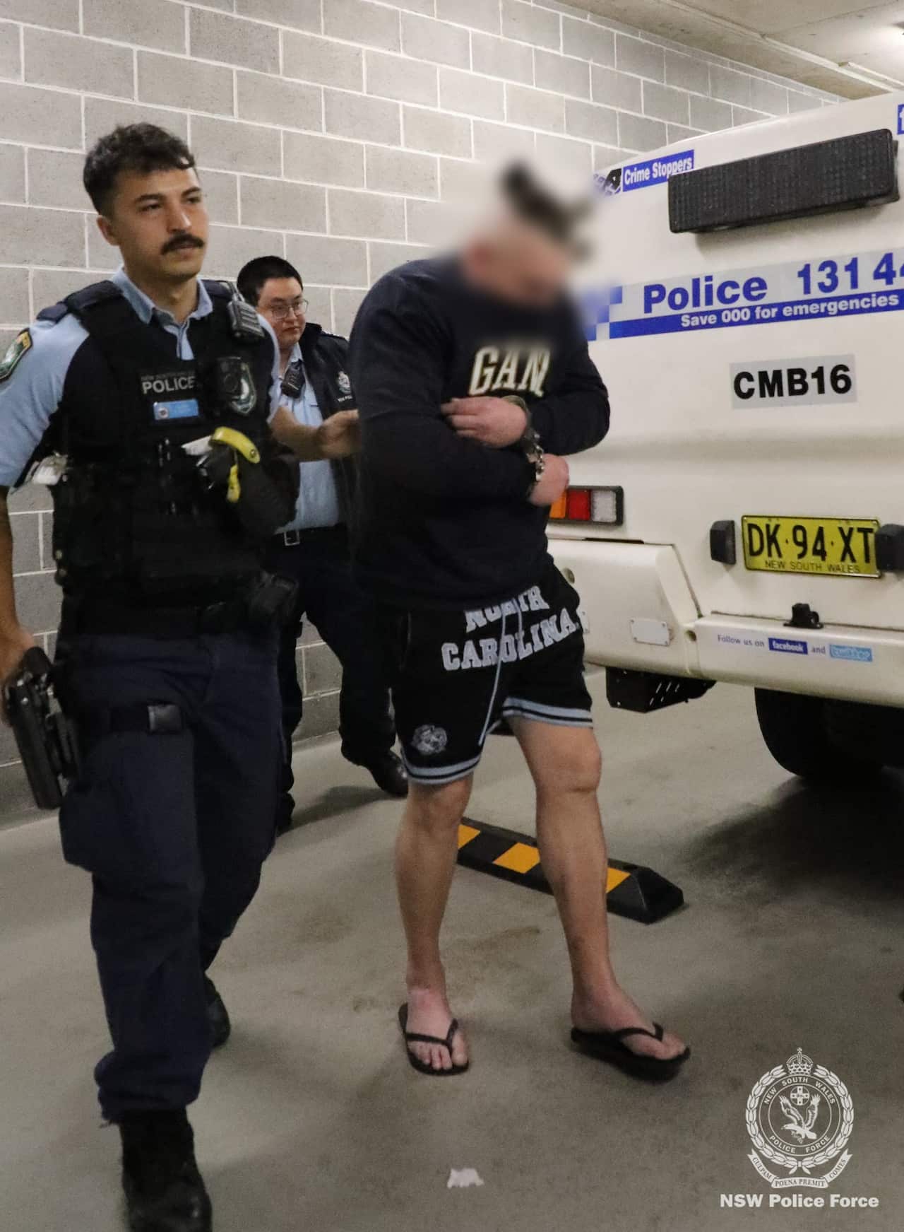 Police escorting a man, who is handcuffed, from a police vehicle.