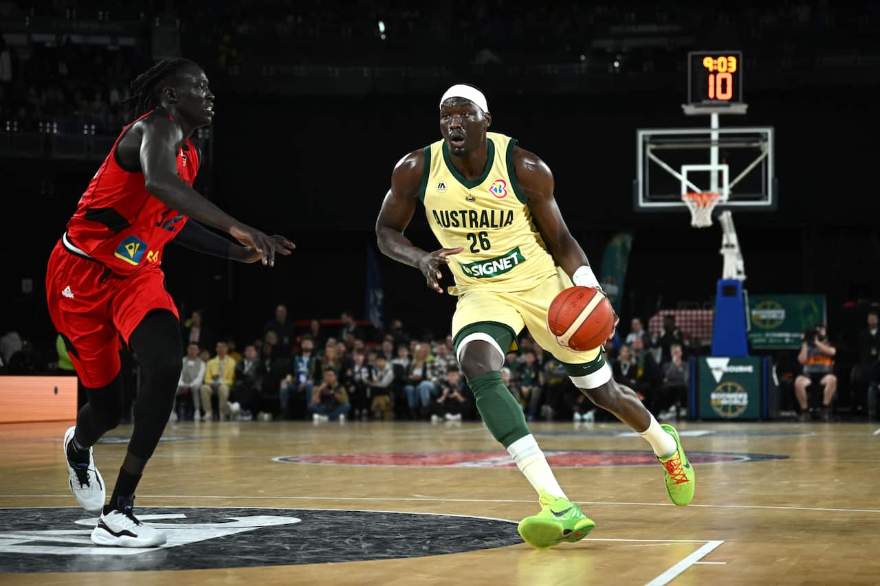 A man in a red basketball uniform runs opposite a man in a yellow basketball uniform holding a ball.