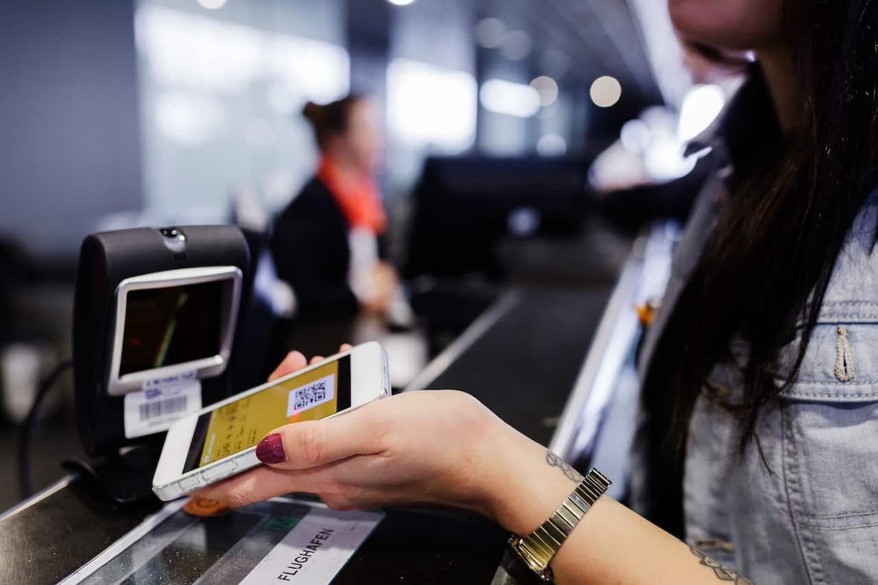 A person's hand holding a phone with a digital boarding pass to a scanner to board their flight.
