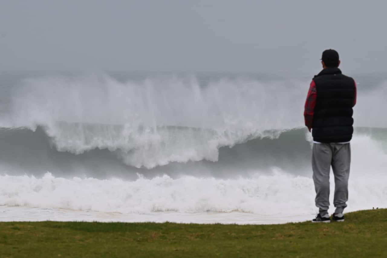 A person looking on as a large swell hits the coast.