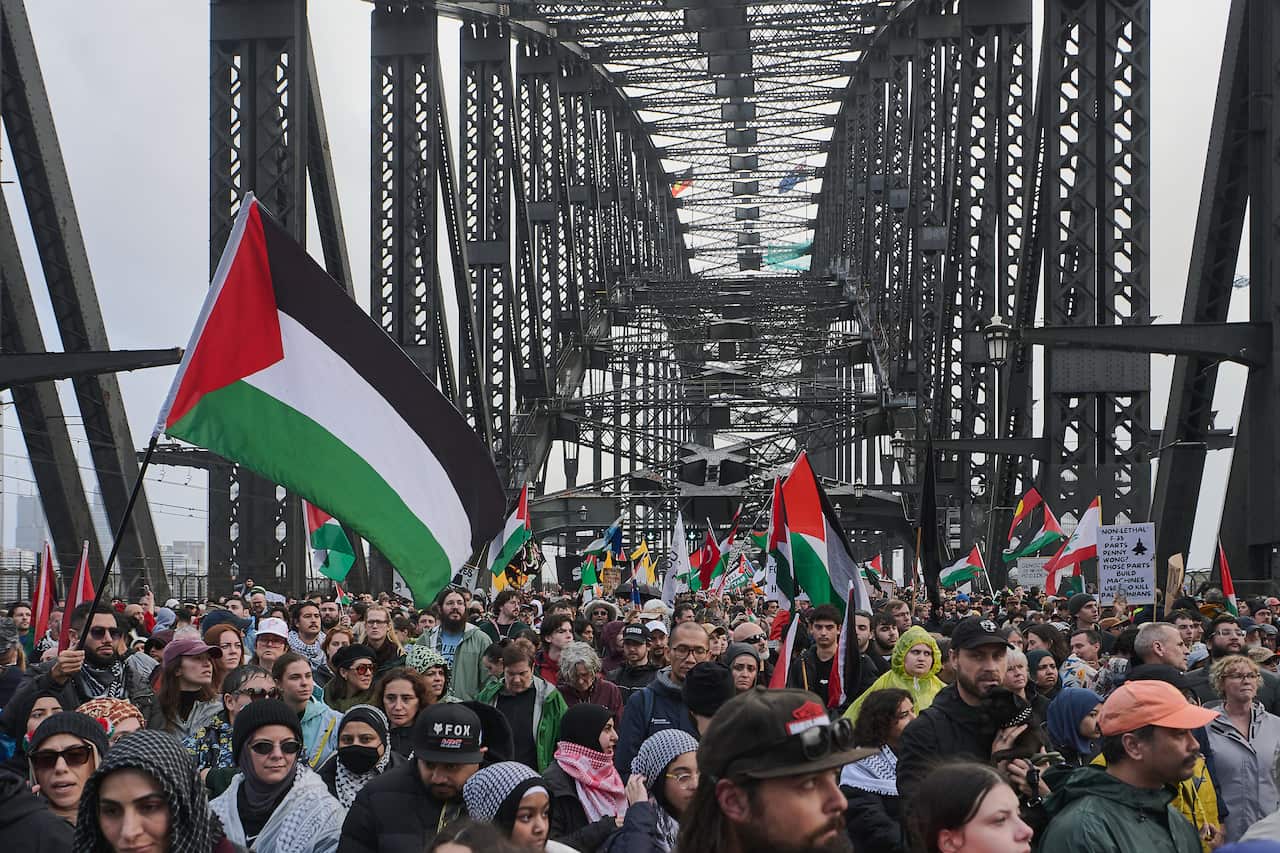 A large crowd of people on Sydney Harbour Bridge. Some are waving Palestinian flags