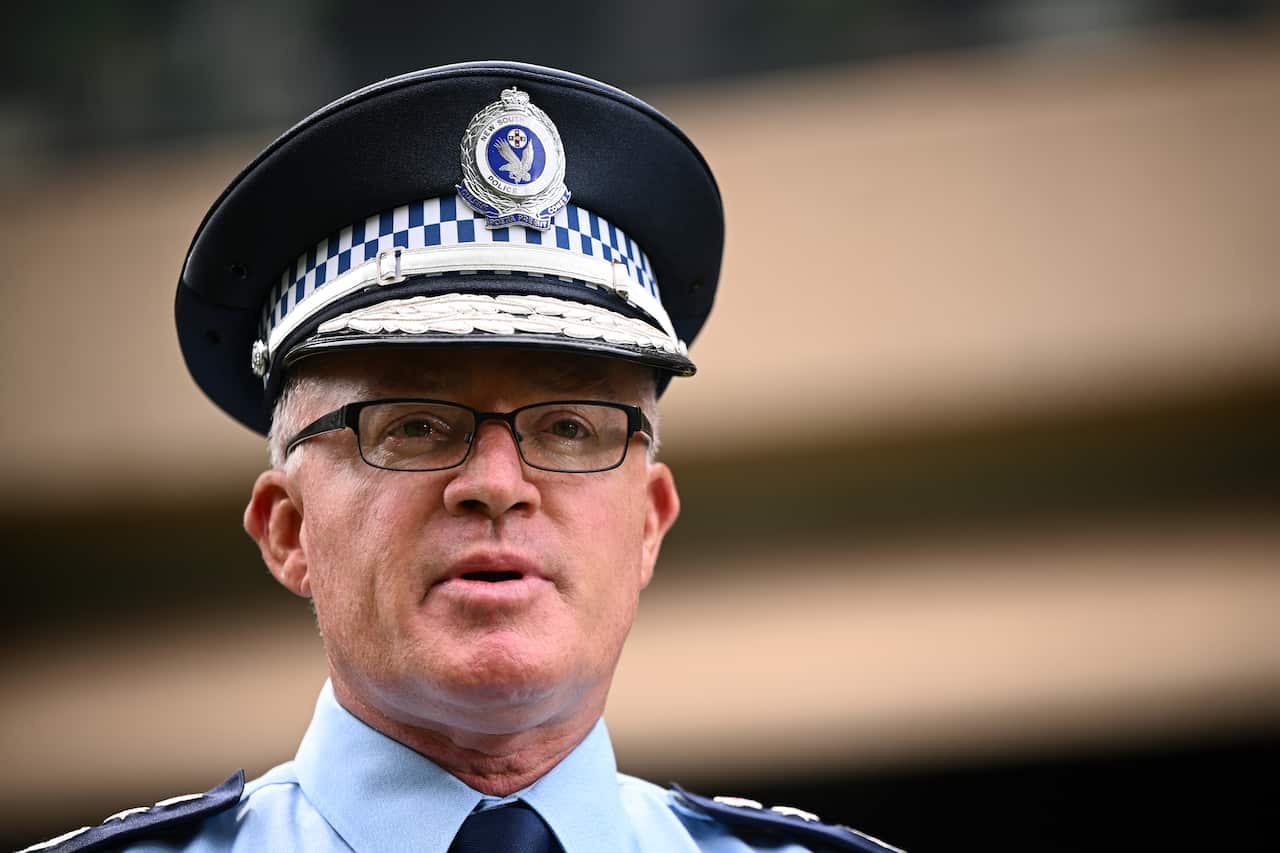 A close-up of a high-ranking NSW Police officer in uniform, wearing a peaked cap with a silver badge and a chequered band.