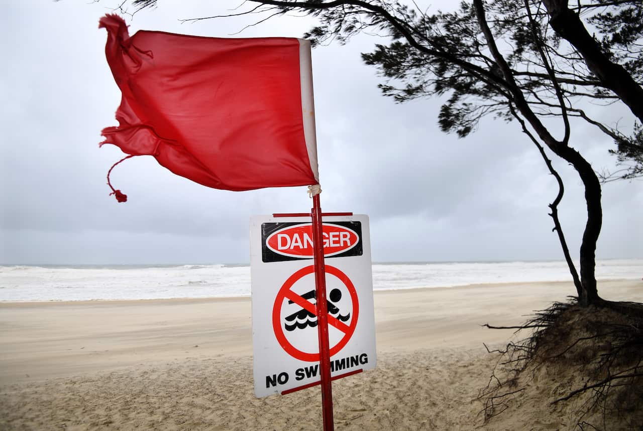 Red flag and “No swimming” danger sign on a windy beach with rough surf.