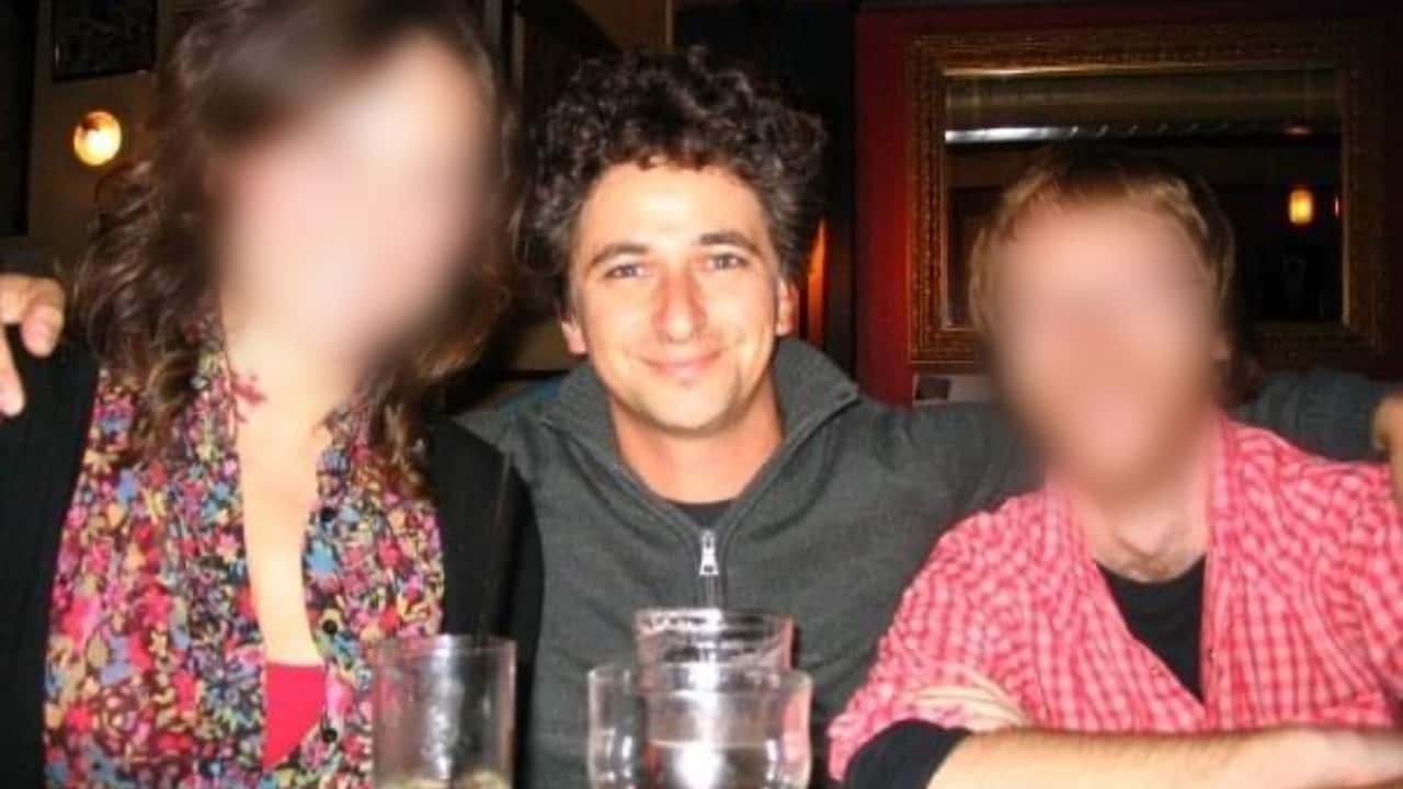 A man is pictured with his arms around friends (whose faces have been blurred) at a pub.