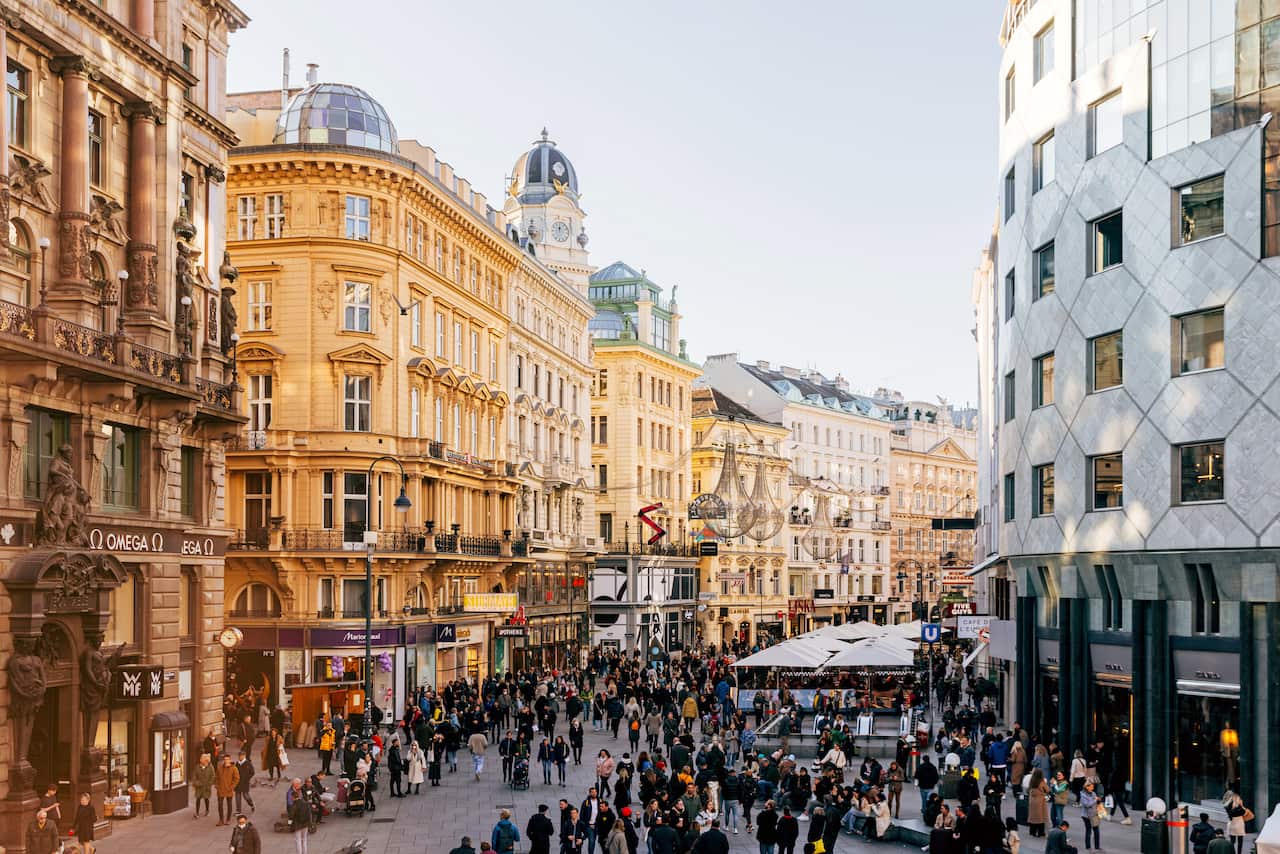 A large group of people walk through a busy road surrounded by large buildings.