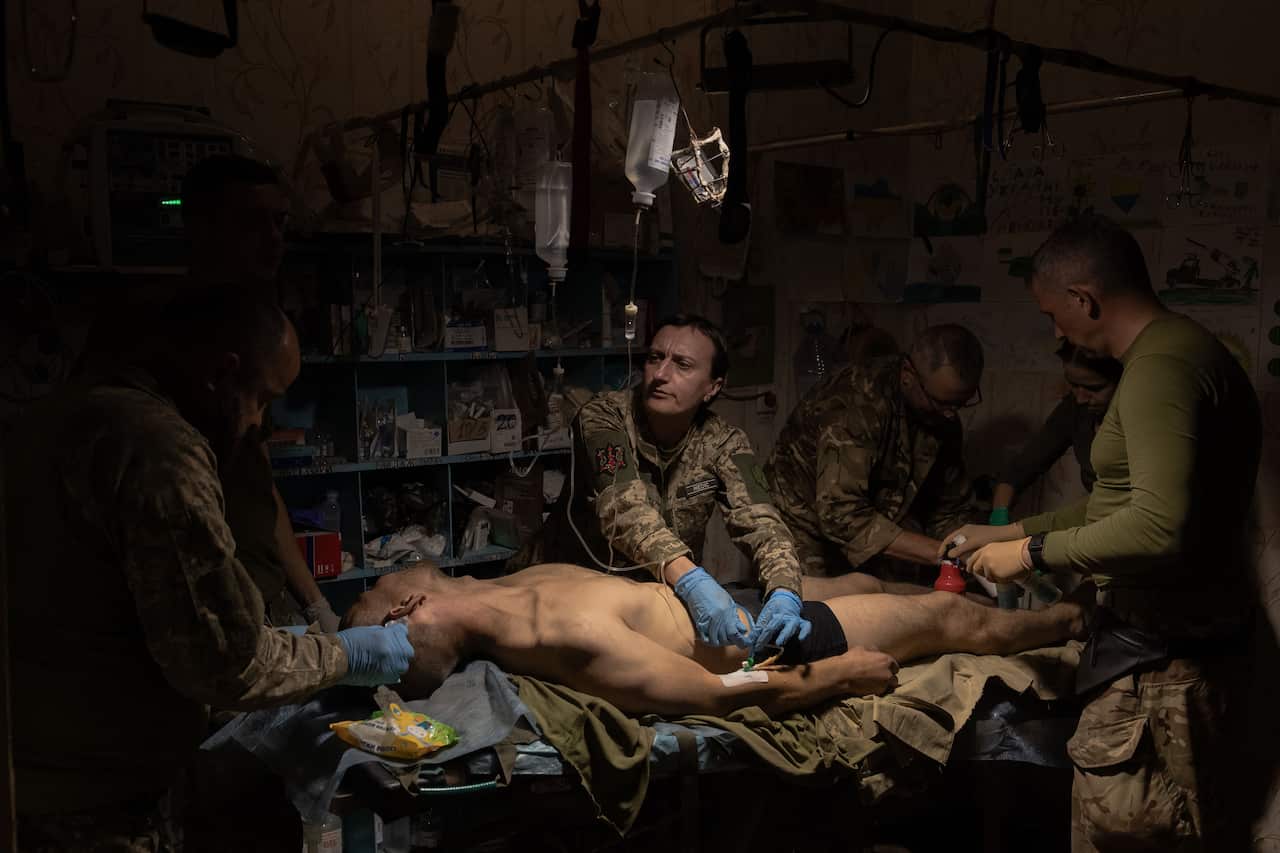 A wounded soldier is seen lying on a stretcher while being tended to in a makeshift hospital.