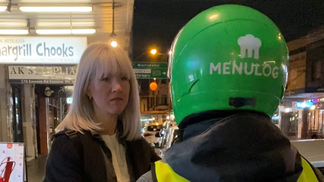 Caucasian white women listens to a delivery rider wearing a green helmet, with his face turned away from the camera. 