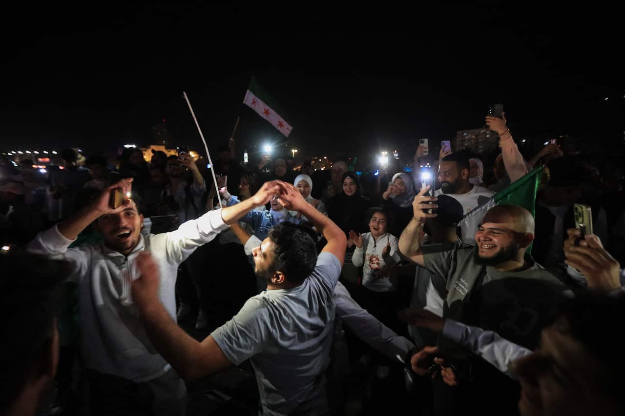 People celebrate by waving Syrian flags on a street.