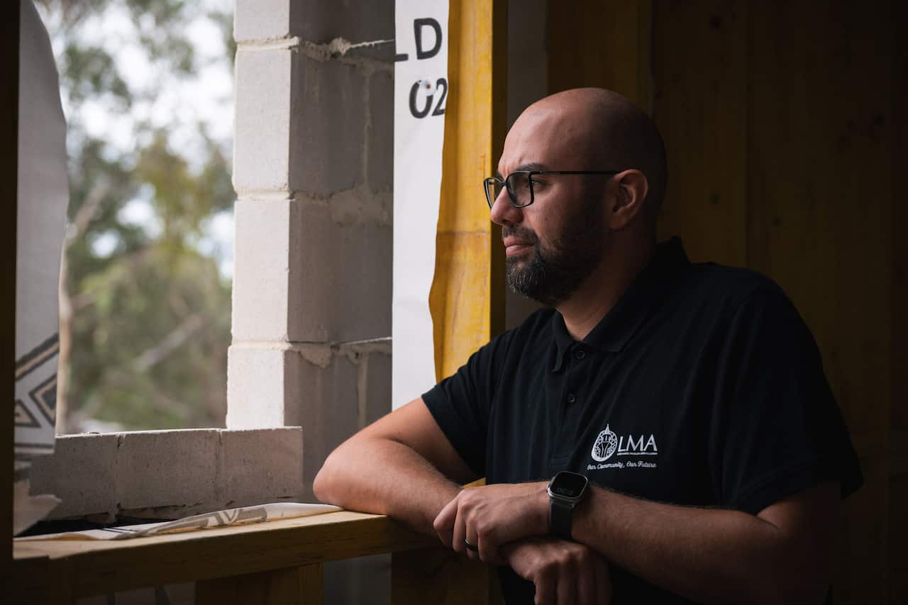 Middle aged man wearing black T shirt rests his elbow on a windowpane