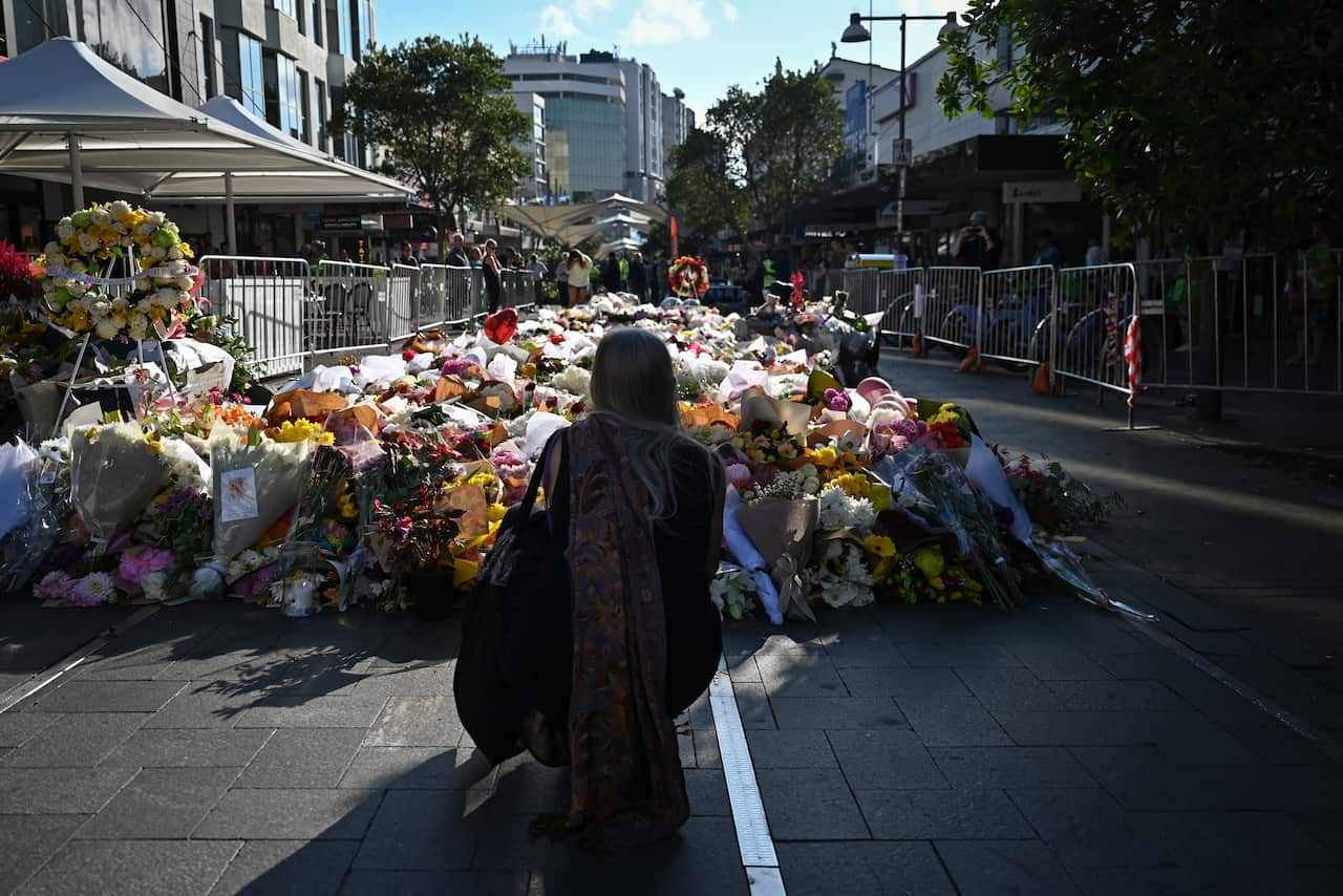 A woman, her back turned, is placing a bouquet among the many flowers already left at the site of the incident.