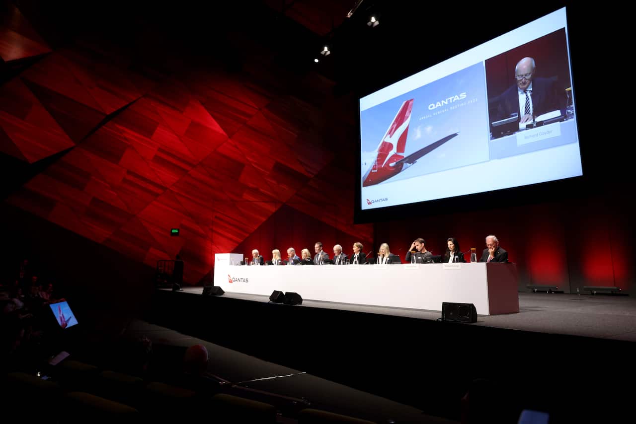 Men and women wearing formal attire seated at a desk on a stage.