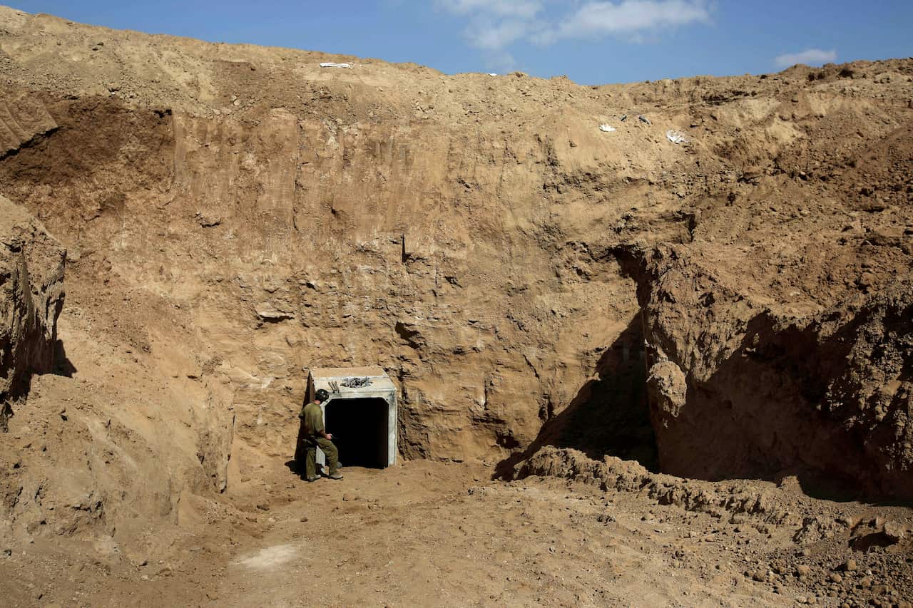 A soldier stands in front of a tunnel entrance in a rock wall.