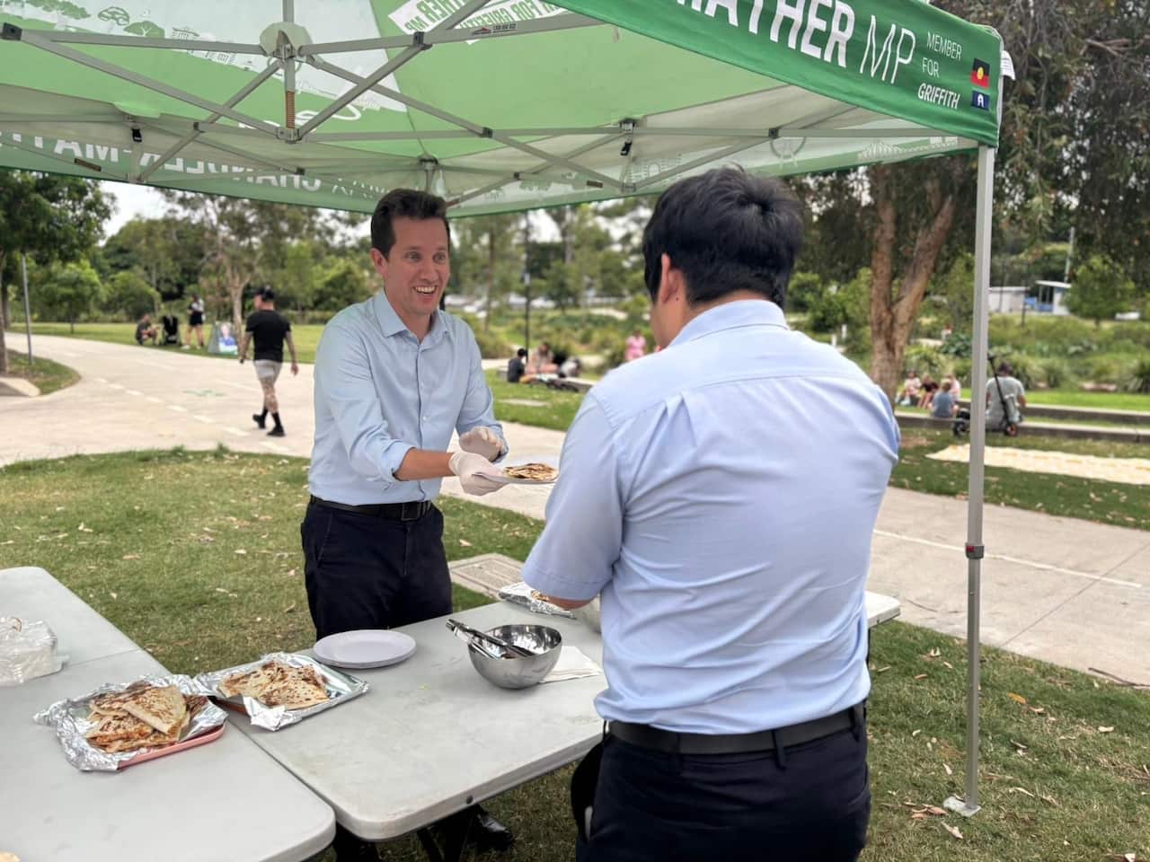 A man serving a quesadilla on a paper plate to another man.