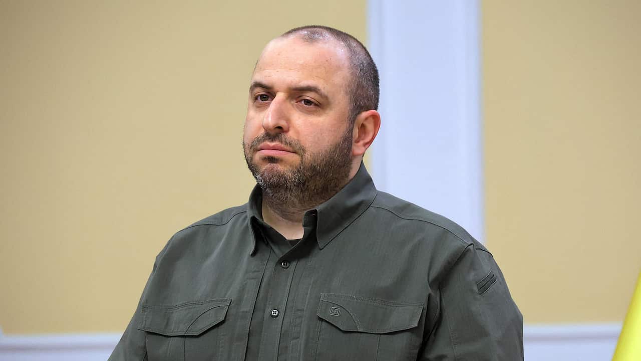 Rustem Umerov in a dark green jacket standing in front of a yellow and white wall.