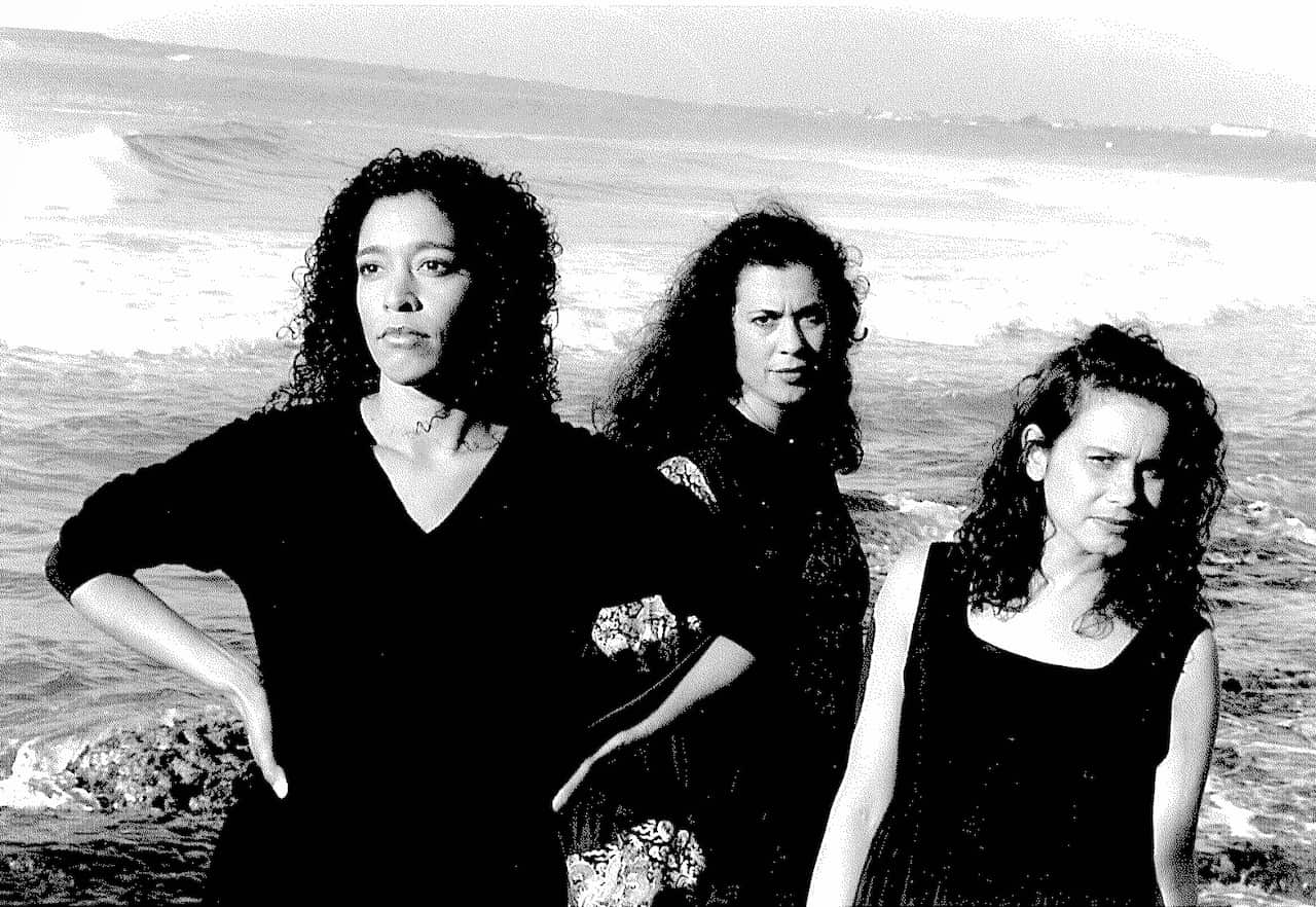Three women posing by the ocean for a photo.