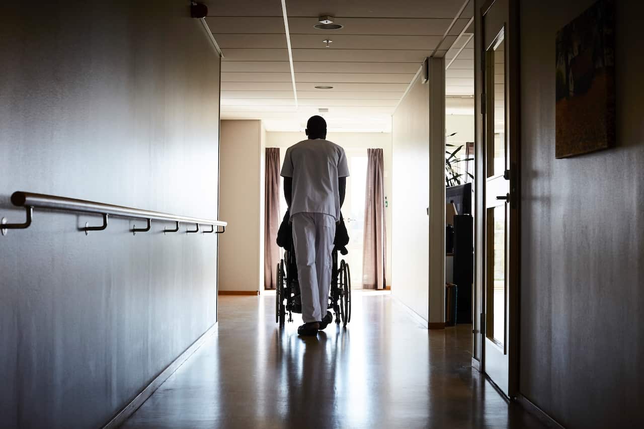 An aged care worker pushing a person in a wheelchair down a corridor