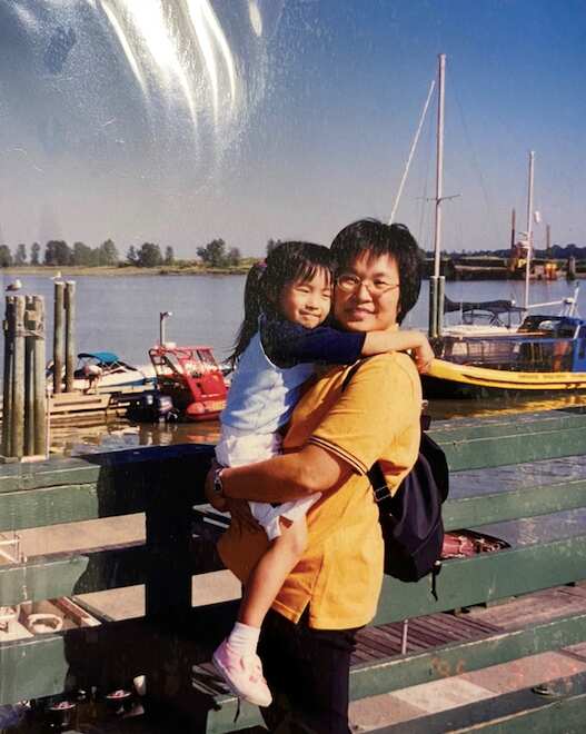 A woman stand in front of some boats floating in the water as she holds a young child and smiles.