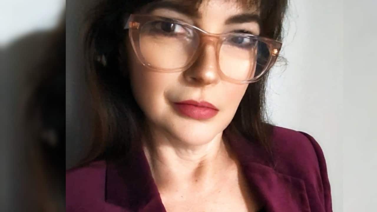a closeup of a middle aged woman in glasses and a maroon jacket