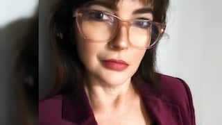 a closeup of a middle aged woman in glasses and a maroon jacket