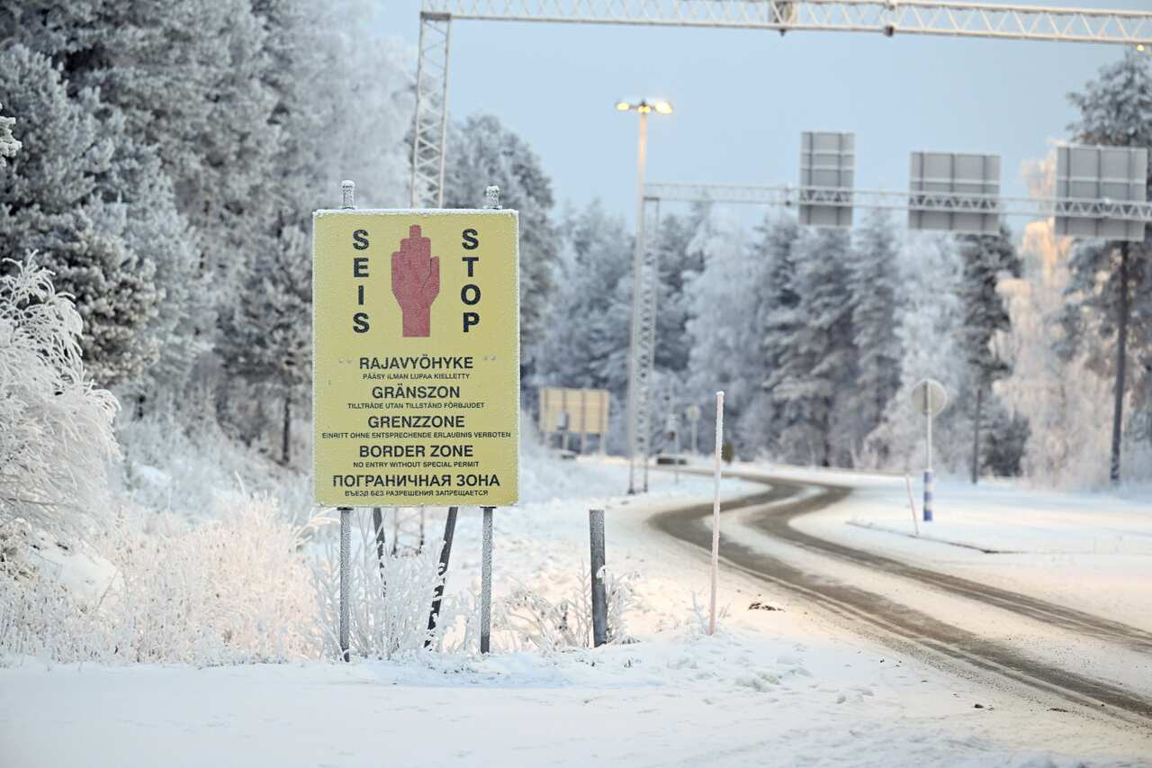 A stop sign leading up to a border crossing next to snow-covered ground.