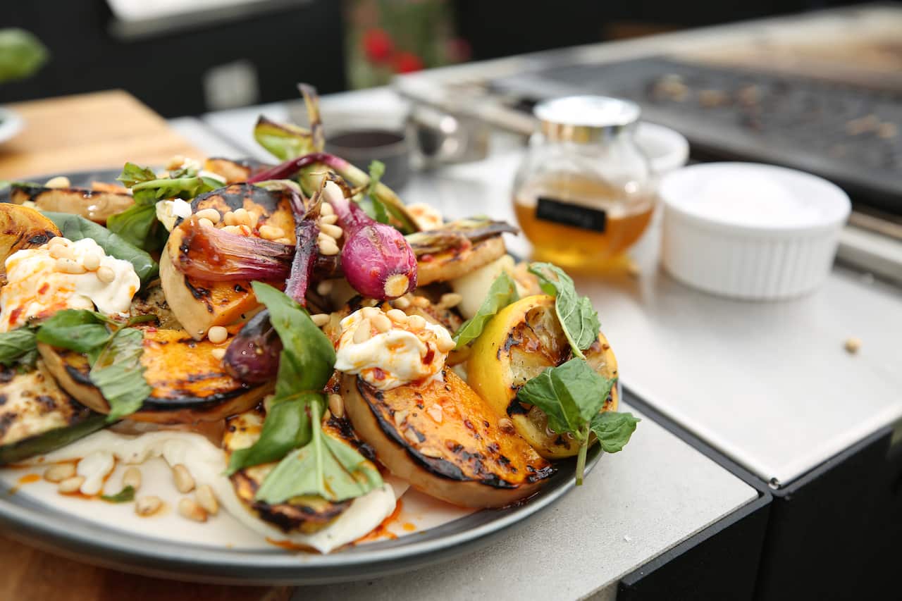 A platter of grilled vegetables sits beside a barbecue grill. 