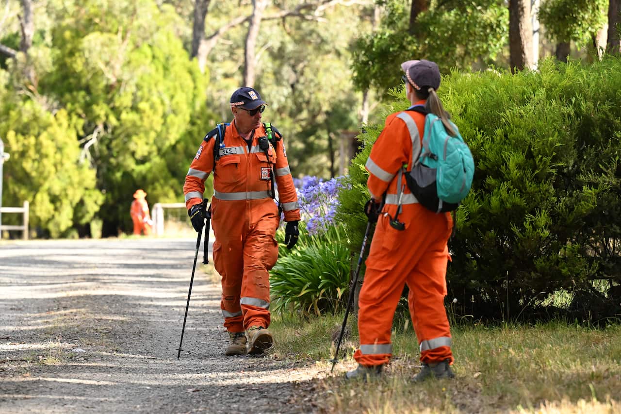 Two SES volunteers in orange uniforms are searching for a missing person.