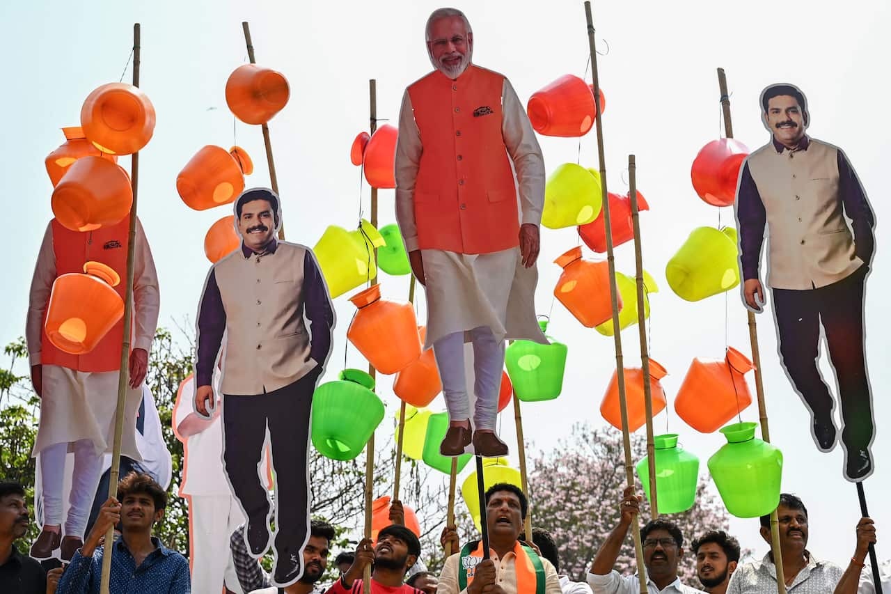 Water pots and cardboard cut-outs of political leaders on sticks are held aloft by a marching crowd. 