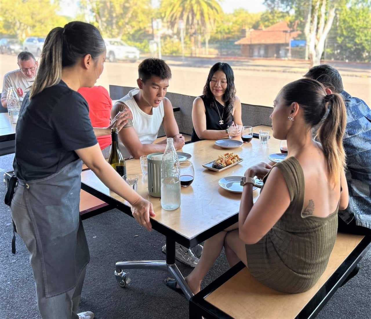 A woman in a black t-shirt serves a group of customers at a restaurant table.