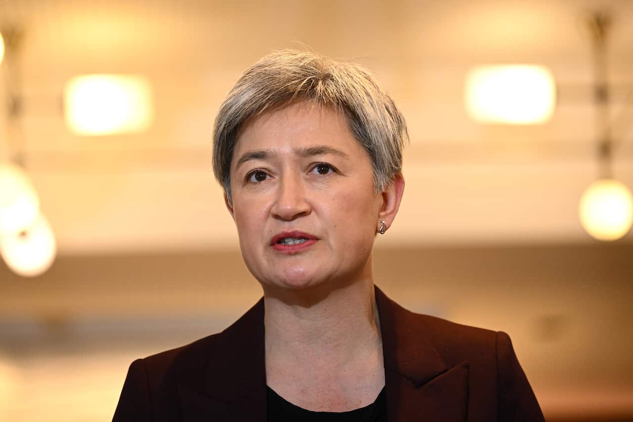 A woman wearing a red coat speaks at a press conference.