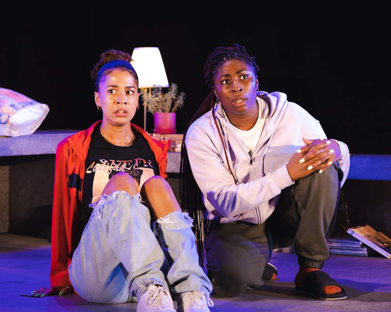 Two women next to each other on stage. One is sitting and the other kneeling.