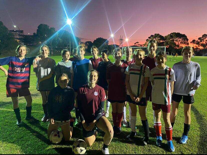 A group photo taken at night on the football pitch of participants in a mentoring workshop.
