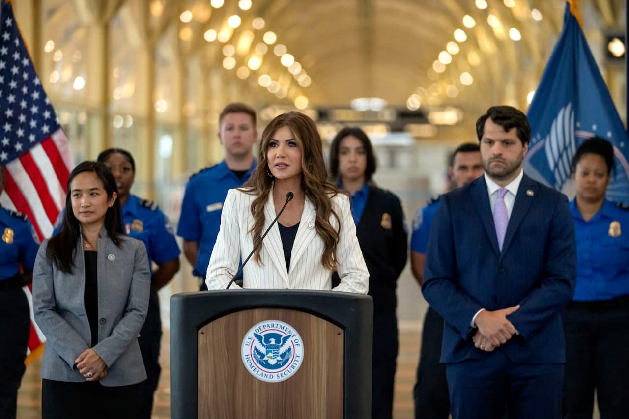 A woman speaking at a podium, surrounded by people in blue uniforms.