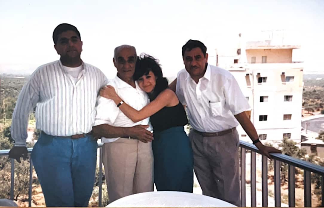An elderly man and a young woman are hugging on a balcony, with men on either side.