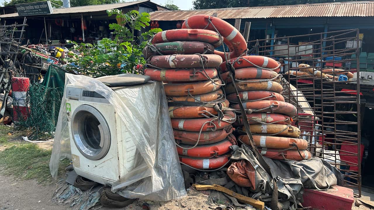 An old washing machine covered in plastic and stacks of orange life-saving rings at a scrapyard