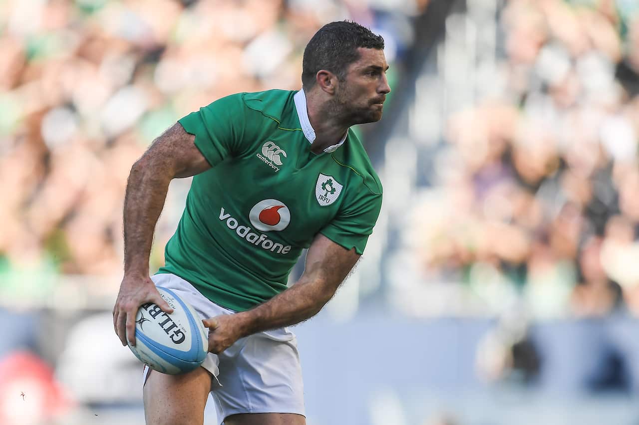 A rugby player in an Ireland shirt and white shorts throws a ball