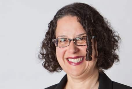 A woman with brown curly hair and glasses smiles