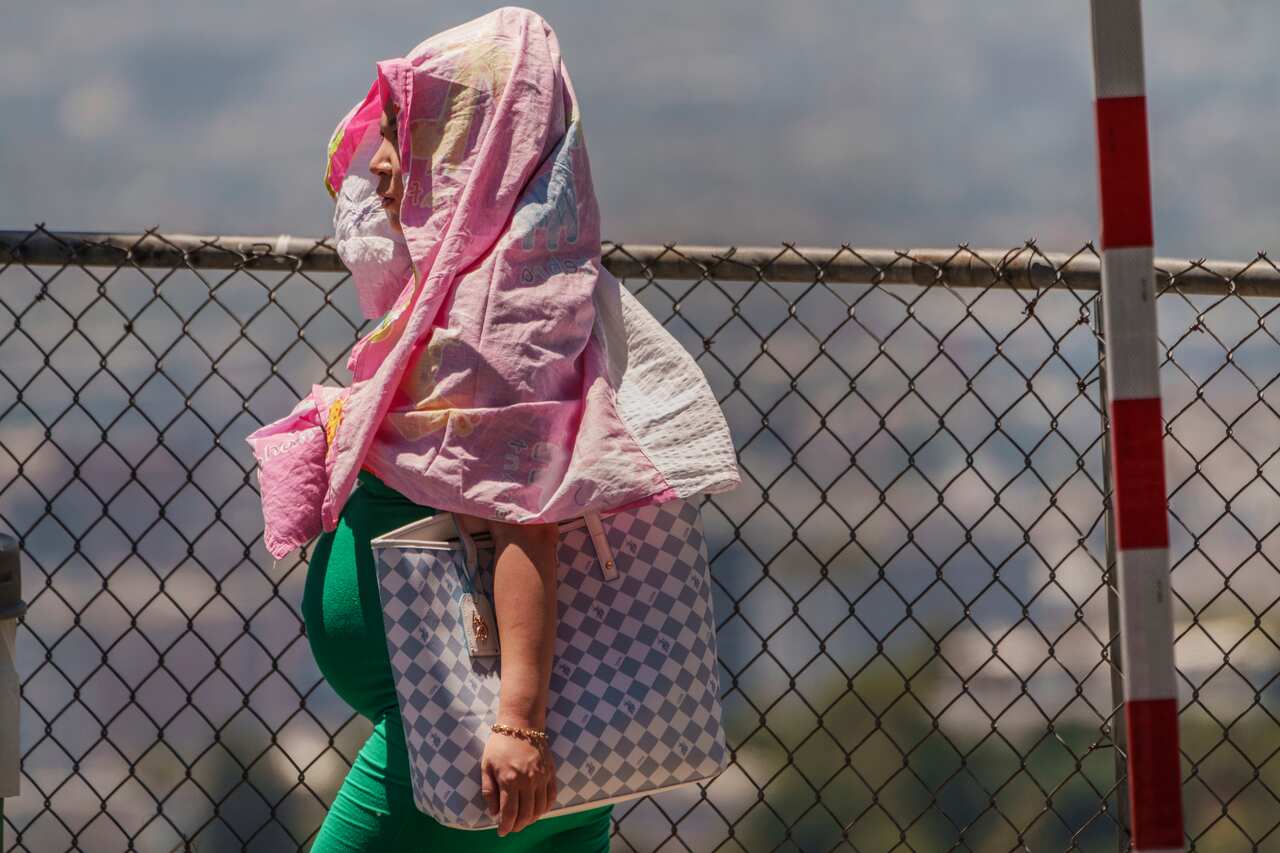 A pregnant woman shields herself from the heat with a shirt covering her head and body.