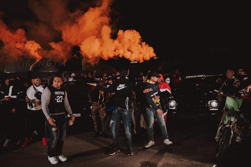 Boys standing next to an orange flare at night. 
