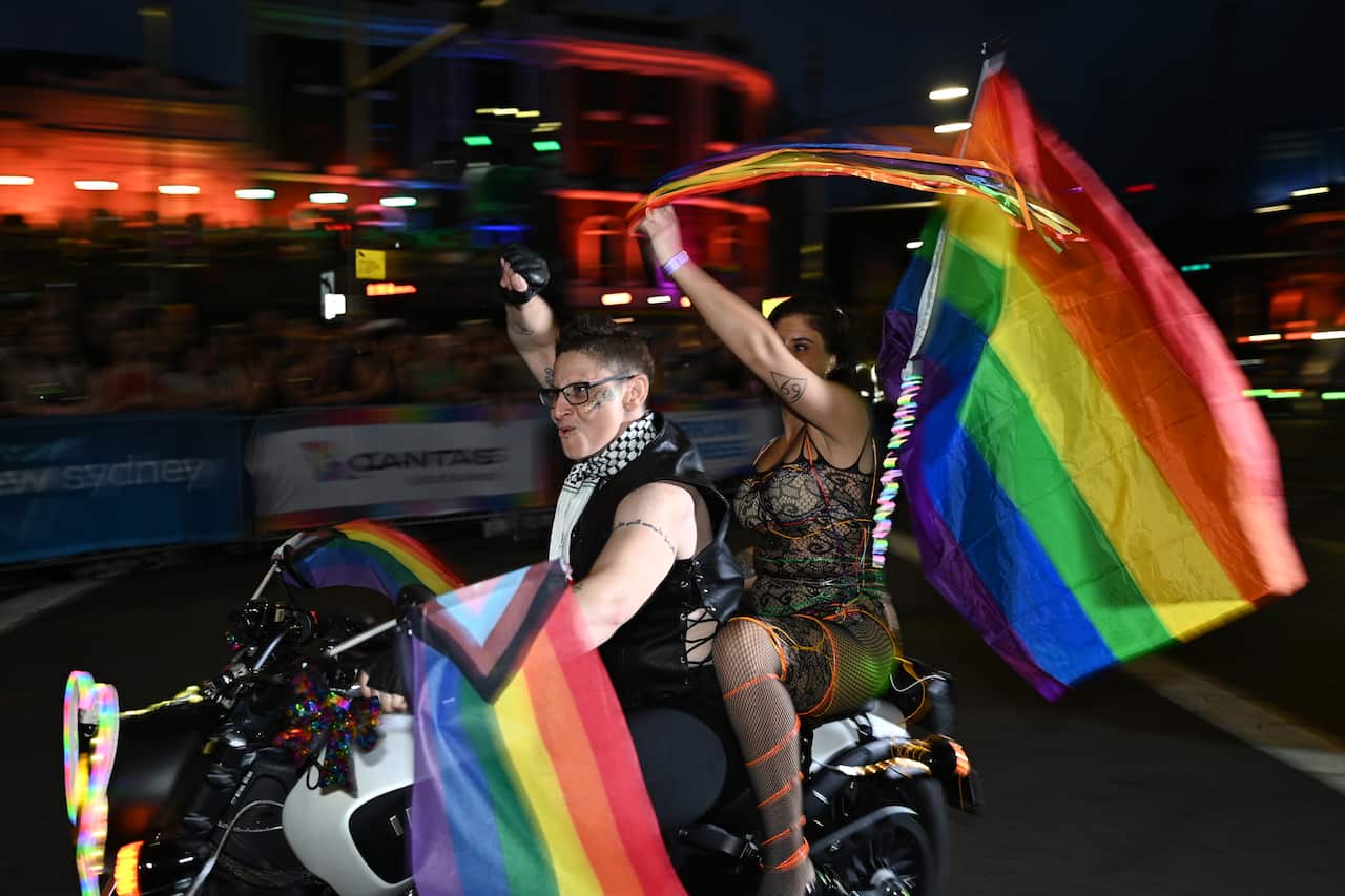 Two people on a motorcycle waving pride flags