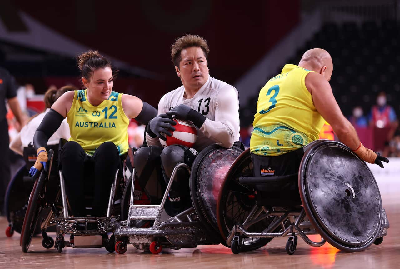 Two Australian wheelchair rugby players surround a Japanese player, who has the ball.