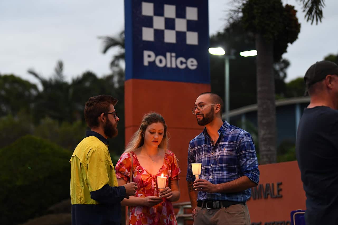 Three people, two of whom are holding candles, standing out the front of a police station.