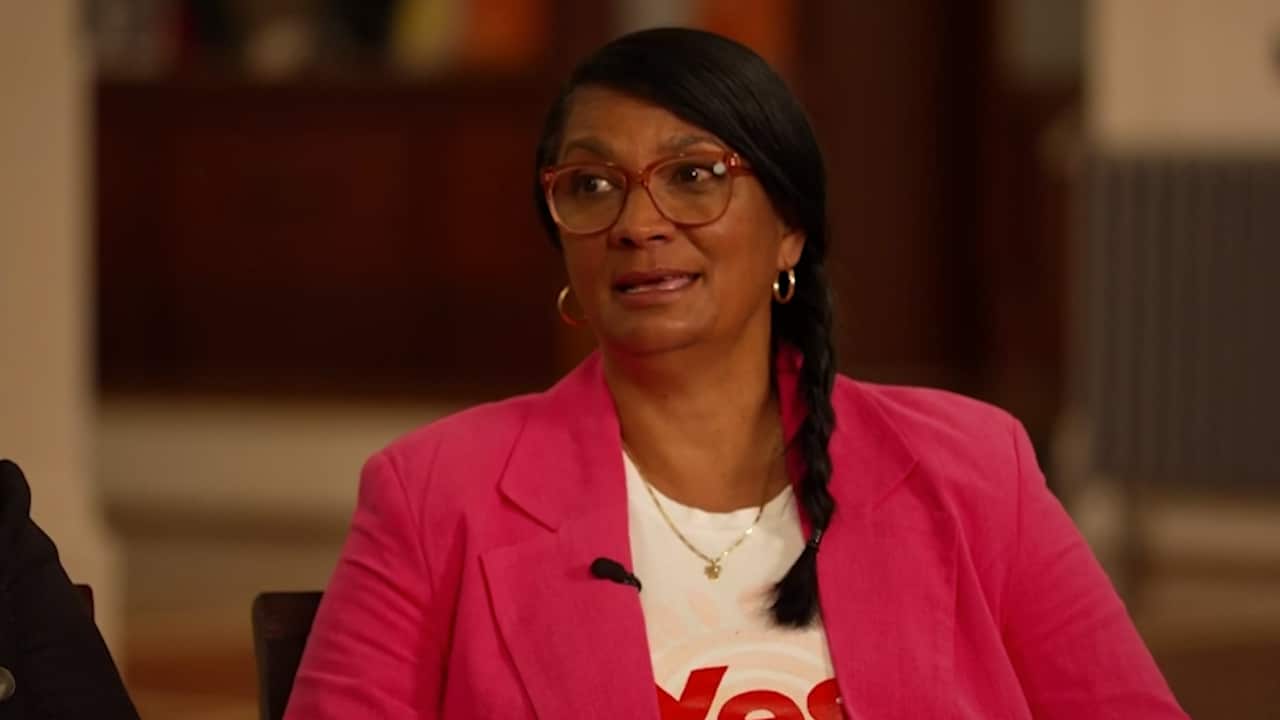 A woman in a white "Yes" shirt and pink blazer.