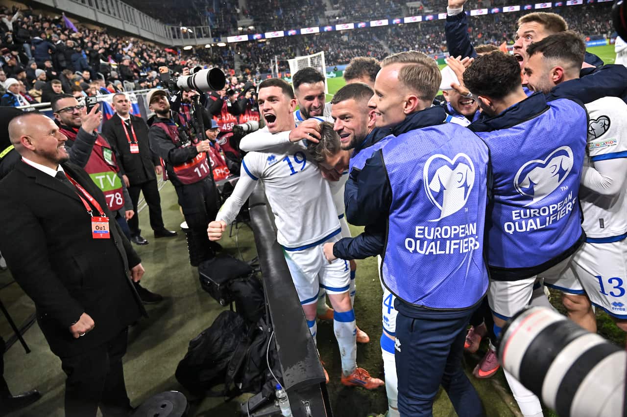 Kosovo's football team wearing white and blue celebrates excitedly at the corner of the field after a victory 