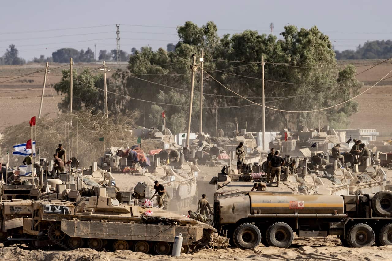 Israeli soldiers organize military equipment while standing on armored personnel carriers near the border with the Gaza Strip.